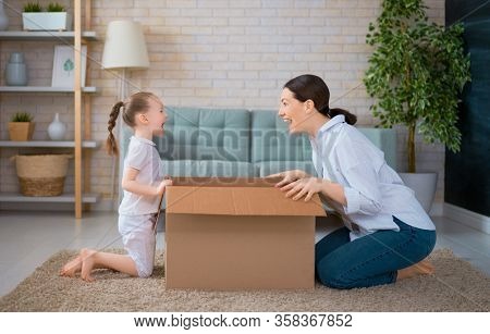 Mother and daughter are unpacking cardboard box at home.                                