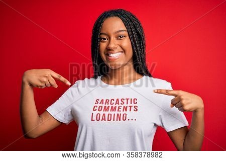 Young african american woman wearing sarcasm coments text on t-shirt over red background very happy pointing with hand and finger