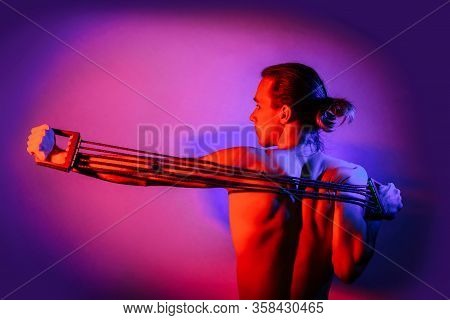 A Young Man Is Training With An Expander, Illuminated By Multi-colored Lights. The Concept Of Sports