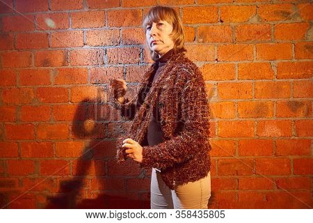 A Middle-aged Woman Poses Showing Clothes Near Red Brick Wall. An Inept Model In An Inept Shoot