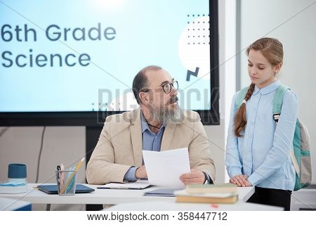 Portrait Of Bearded Senior Teacher Talking To Cute Schoolgirl While Grading Test In Science Class, C