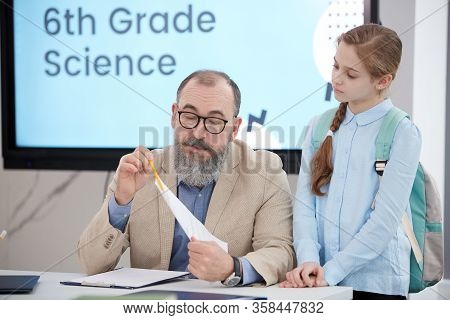 Portrait Of Bearded Senior Teacher Talking To Cute Schoolgirl While Grading Test In Class, Copy Spac