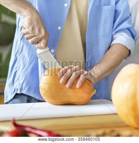 Unrecognizable Caucasian Man Chopping Pumpkin On A Board For Cooking Vegetarian Dessert
