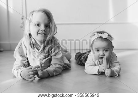 Two Cute Sisters Sitting On Floor And Playing At Home.little Sister Hugging Her Smalest Sister. Todd