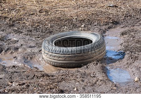 A Worn Car Tire Is Wallowing In Mud And A Puddle On The Ground. Environmental Pollution. Ecological