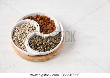 Peeled Sunflower Seeds, Pumpkin Seeds And Raisins Lie On A White Table In A Beautiful Round Plate Di