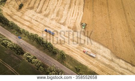 Aerial View Of A Combine That Unloads Grain From Its Grain Compartment Into A Truck Van. One Truck D