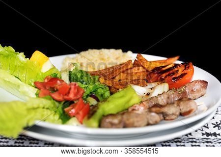 Traditional Turkish Lunch. Grilled Lamb Kebab On Wooden Skewers, Fried Potatoes And Side Dish On Tab