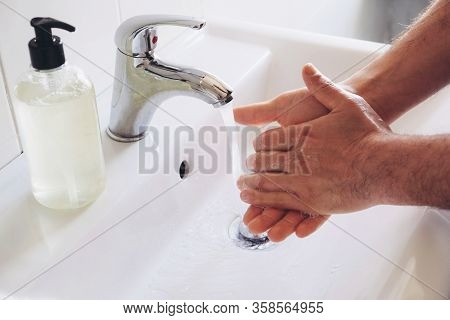 Man Cleaning His Hands Using Liquid Disinfectant Soap And Water In Bathroom