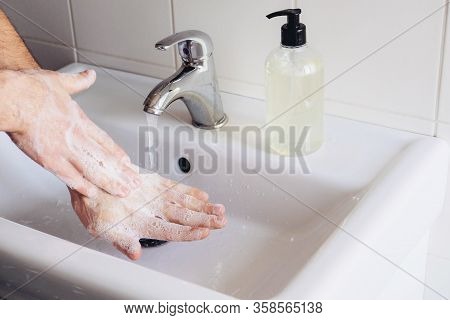 Man Cleaning His Hands Using Liquid Disinfectant Soap And Water In Bathroom.