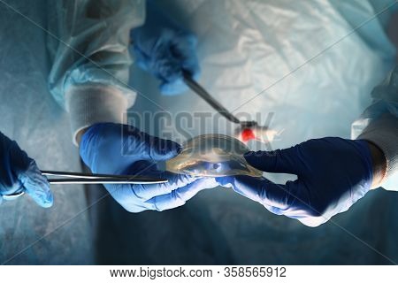 Surgeons Holding Instruments And Breast Implant. Plastic Surgeon Offers Breast Implant Based On His 