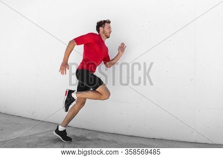 Running man jogging fast profile sideways against white wall outdoor background. Male athlete training healthy active lifestyle.