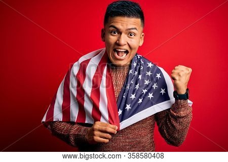 Young handsome latin patriotic man wearing united states of america falg screaming proud and celebrating victory and success very excited, cheering emotion