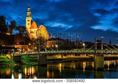 Salzburg night view - Leprosenhauskirche church and Mullner Steg bridge illuminated at night. Salzburg, Austria