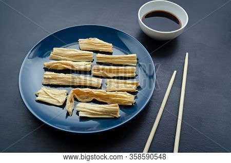 Soy Tofu Yuba Skin On A Blue Plate With Bamboo Sticks And Soy Sauce On A Black Slate Background. Eas
