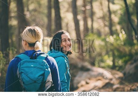 Two Girls With Backpacks Walk In The Woods. Hiking In The Mountains. Girlfriends Spend Time Together