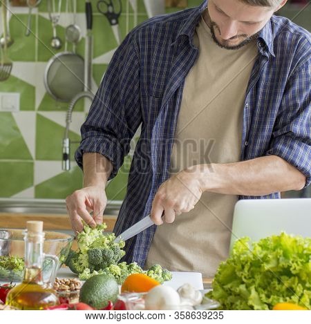 Young Man Preparing Vegetable Salad In Bowl And Suggesting To Eat Healthy Food, Kitchen Background