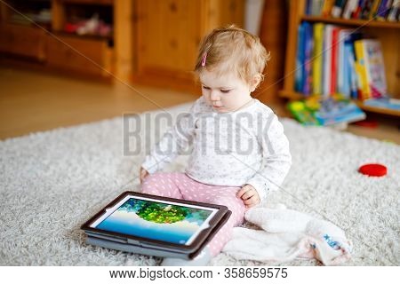 Cute Adorable Baby Girl Watching Cartoons On Tablet Pc. Todder Child At Home Touching On Screen And 