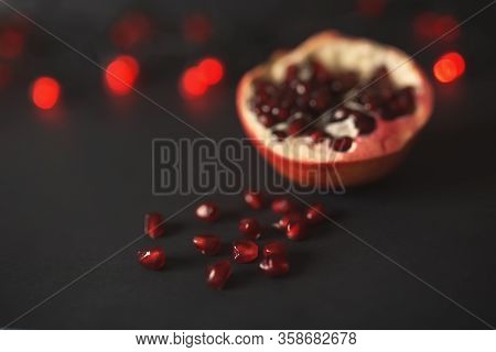 Ripe Beautiful Cut Pomegranate On A Black Background With Red Lanterns. Pomegranate Seeds Are Scatte