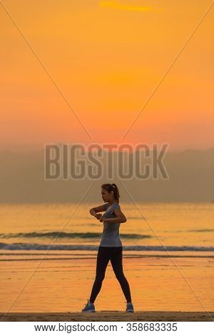 Woman Standing And Exercise On Beanch In The Morning With Colorful Sky And Wave In Background.