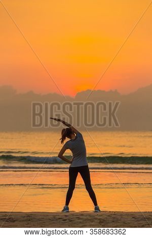 Woman Standing And Exercise On Beanch In The Morning With Colorful Sky And Wave In Background.