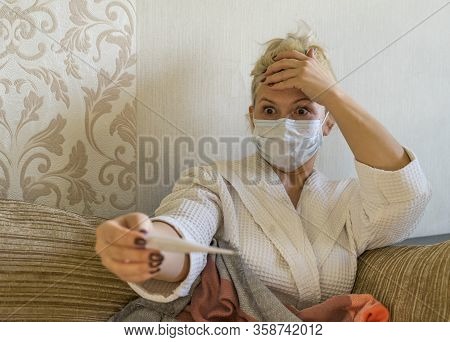 A Woman In A Medical Mask Stares Wide - Eyed At A Thermometer. Stay At Home. Stay Safe.