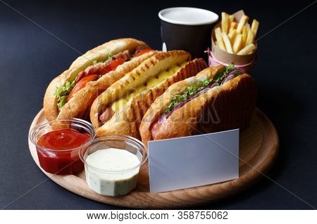 Three Hot Dogs, Sause, Ketchup, Coffee, French Fries Lying On The Wooden Plate.