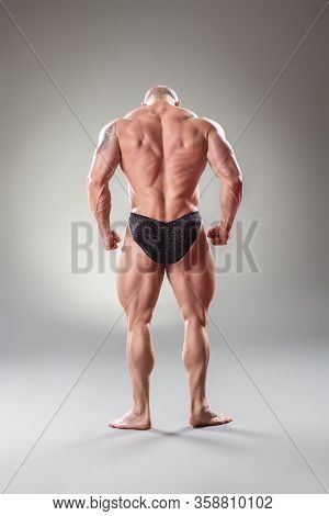 Sexy Muscular Bodybuider Posing On The Gray Background. Back View