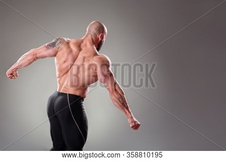 Sexy Muscular Bodybuider Posing On The Gray Background. Triceps And Back Contraction
