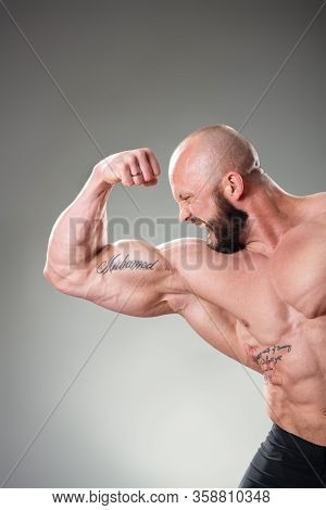 Sexy Muscular Bodybuider Posing On The Gray Background. Biceps Contraction