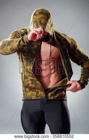 Sexy Muscular Bodybuider Posing With Sweatshirt And Hood On The Gray Background