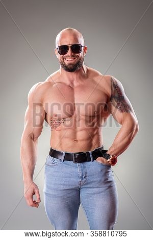 Sexy Muscular Bodybuider With Sunglasses Posing On The Gray Background