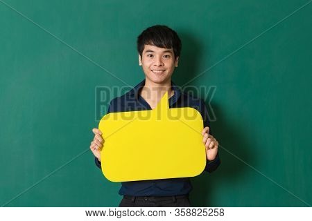 Young And Handsome Cute Asian Man Standing At Dark Green Wall,  Holding And Showing Colorful Blank S