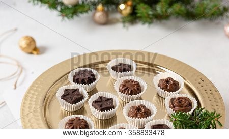 Raw Vegan Handmade Chocolate Candies On Golden Tray On White Concrete Background With Fir Branches. 