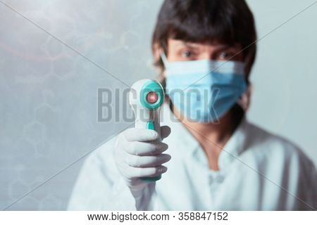 Doctor Wearing Protective  Mask Ready To Use Infrared Forehead Thermometer  To Check Body Temperatur