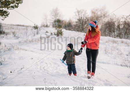 Mother And Little Toddler Boy Walking In The Winter Forest And Having Fun With Snow. Family Enjoying