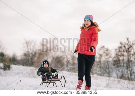 A Father Is Carrying A Child On A Sled. Father Walks With Her Son Over The Snow-covered Forest. Chee
