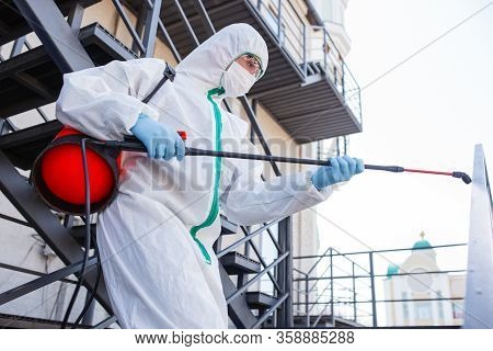 Coronavirus Pandemic. A Disinfector In A Protective Suit And Mask Sprays Disinfectants In House Or O