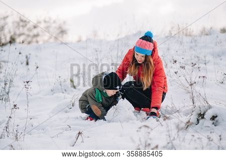 Mother And Little Toddler Boy Walking In The Winter Forest And Having Fun With Snow. Family Enjoying