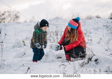 Mother And Little Toddler Boy Walking In The Winter Forest And Having Fun With Snow. Family Enjoying