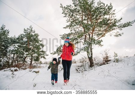 Mother And Little Toddler Boy Walking In The Winter Forest And Having Fun With Snow. Family Enjoying