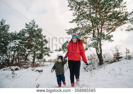 Mother And Little Toddler Boy Walking In The Winter Forest And Having Fun With Snow. Family Enjoying