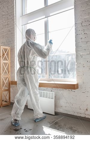 Coronavirus Pandemic. A Disinfector In A Protective Suit And Mask Sprays Disinfectants In House Or O