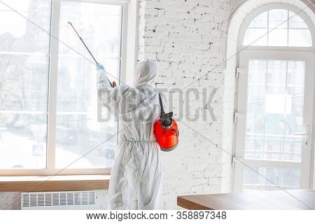 Coronavirus Pandemic. A Disinfector In A Protective Suit And Mask Sprays Disinfectants In House Or O