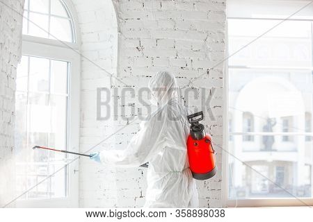 Coronavirus Pandemic. A Disinfector In A Protective Suit And Mask Sprays Disinfectants In House Or O