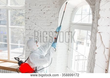Coronavirus Pandemic. A Disinfector In A Protective Suit And Mask Sprays Disinfectants In House Or O