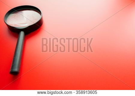 Close Up Single Magnifying Glass With Black Handle, Leaning On The Red Table At The Office.