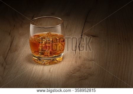 On The Wooden Table Is A Glass Of Whiskey On The Rocks. Space For Text.