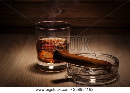 A Smoking Cigar And A Glass Of Whiskey On A Wooden Table. Space For Text.