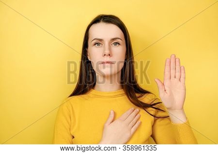 Honest Serious Young Brunette Woman Swears To Do Something, Keeps Hand On Chest, Gestures With Palm,